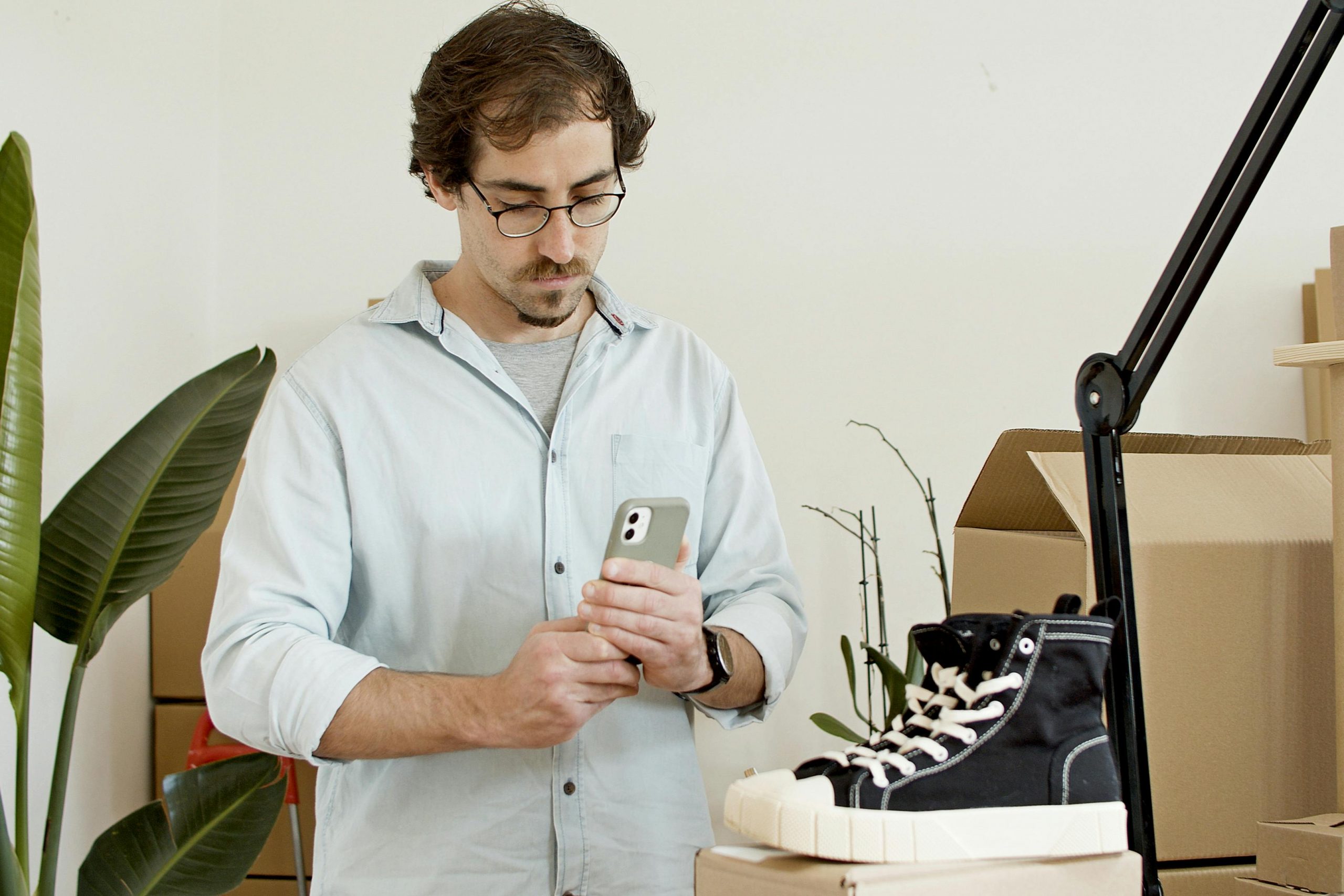 man using a smartphone beside stacked cardboard boxes, with a pair of shoes resting on the top box