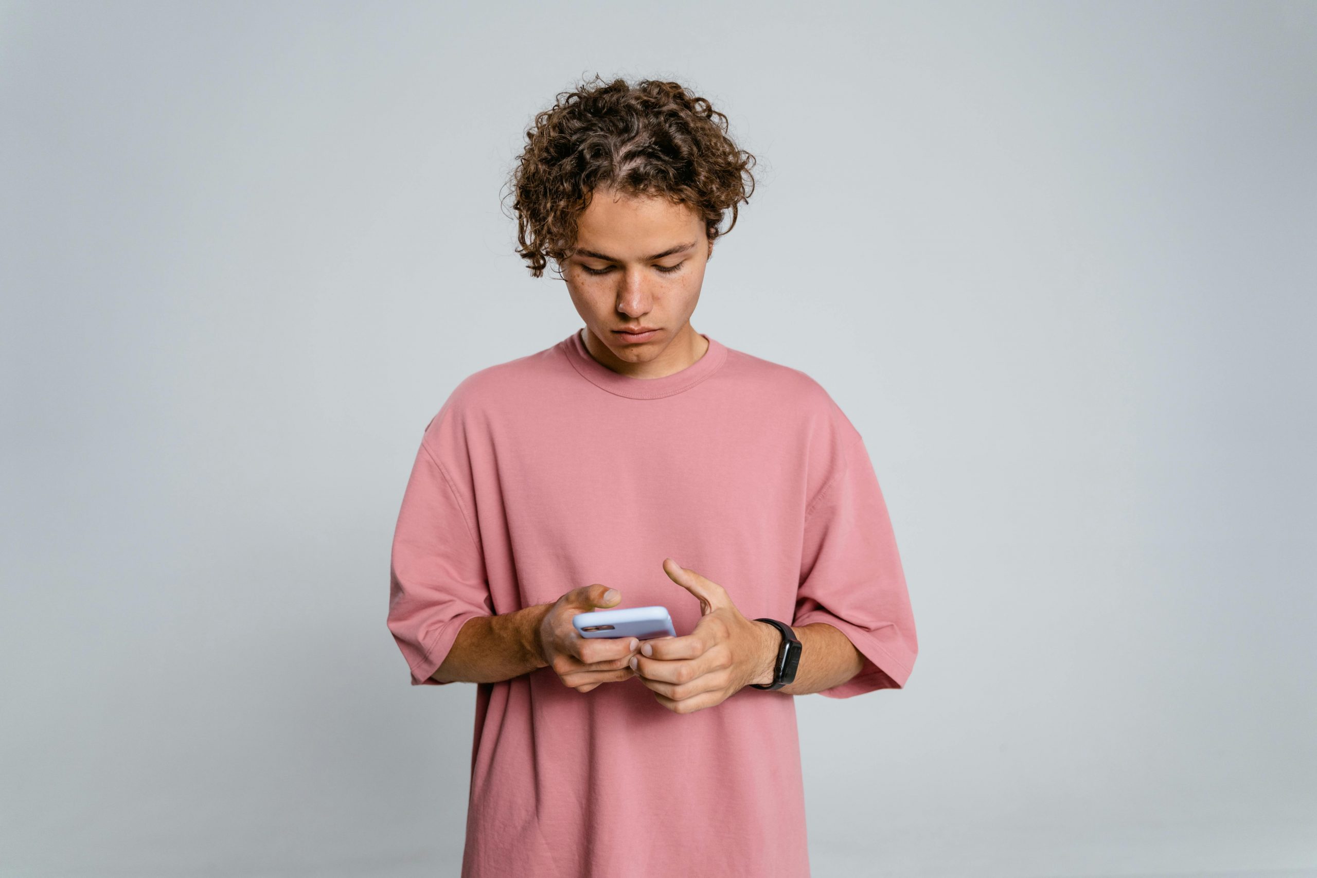 young man in a pink shirt focused on his smartphone