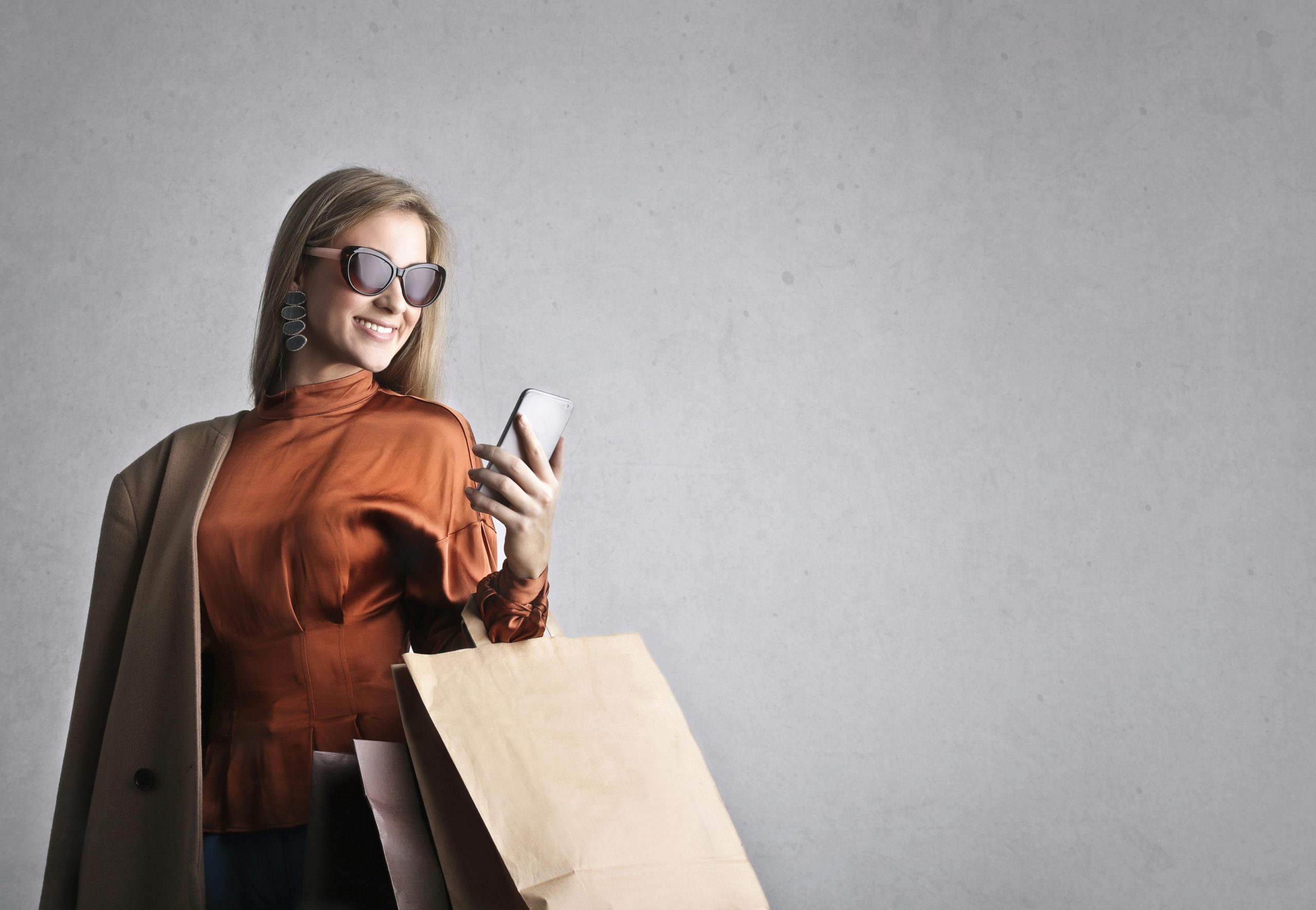woman wearing sunglasses carrying shopping bags and using a smartphone