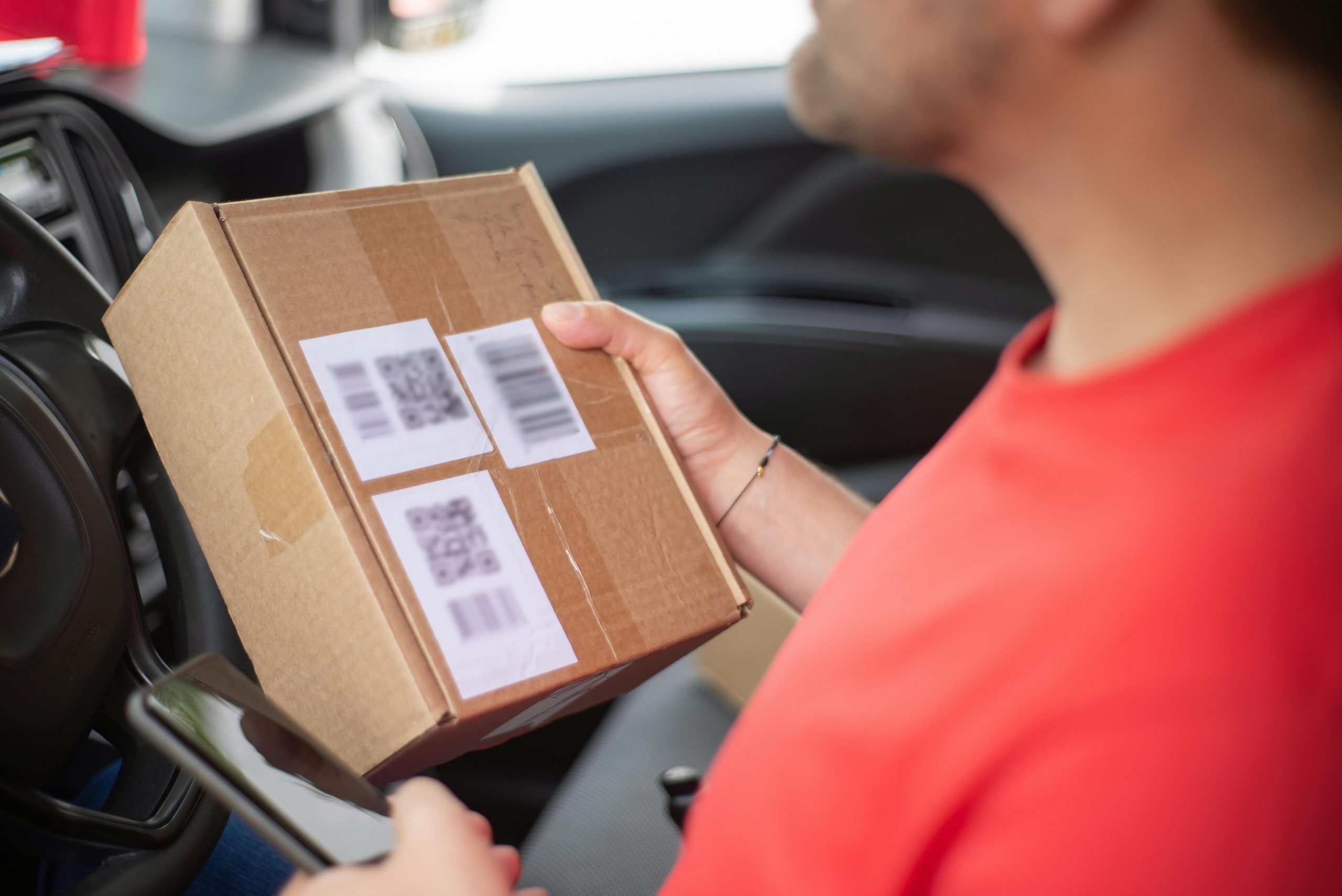 delivery worker sitting in a van, holding a parcel and using his phone
