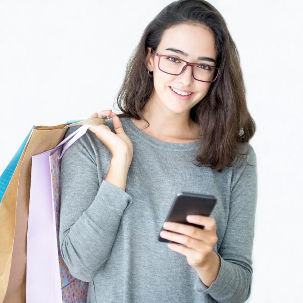 woman wearing glasses, carrying shopping bags in one hand and holding a smartphone in the other