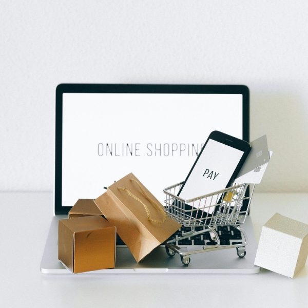 miniature boxes and a small shopping cart holding a smartphone with the word "pay" on the screen, with a laptop in the background displaying "online shopping"